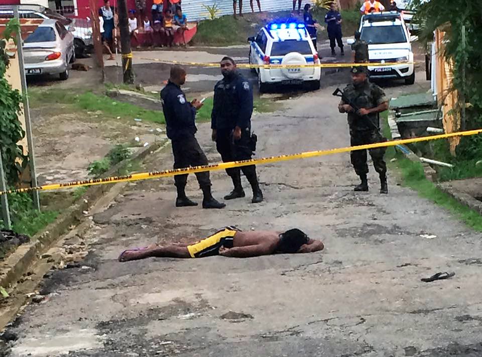 DEAD END: Police and soldiers stand near the body of Kirwin Williams who was shot dead on Wednesday afternoon outside his Laventille home. Williams’ elderly neighbour was also shot.
