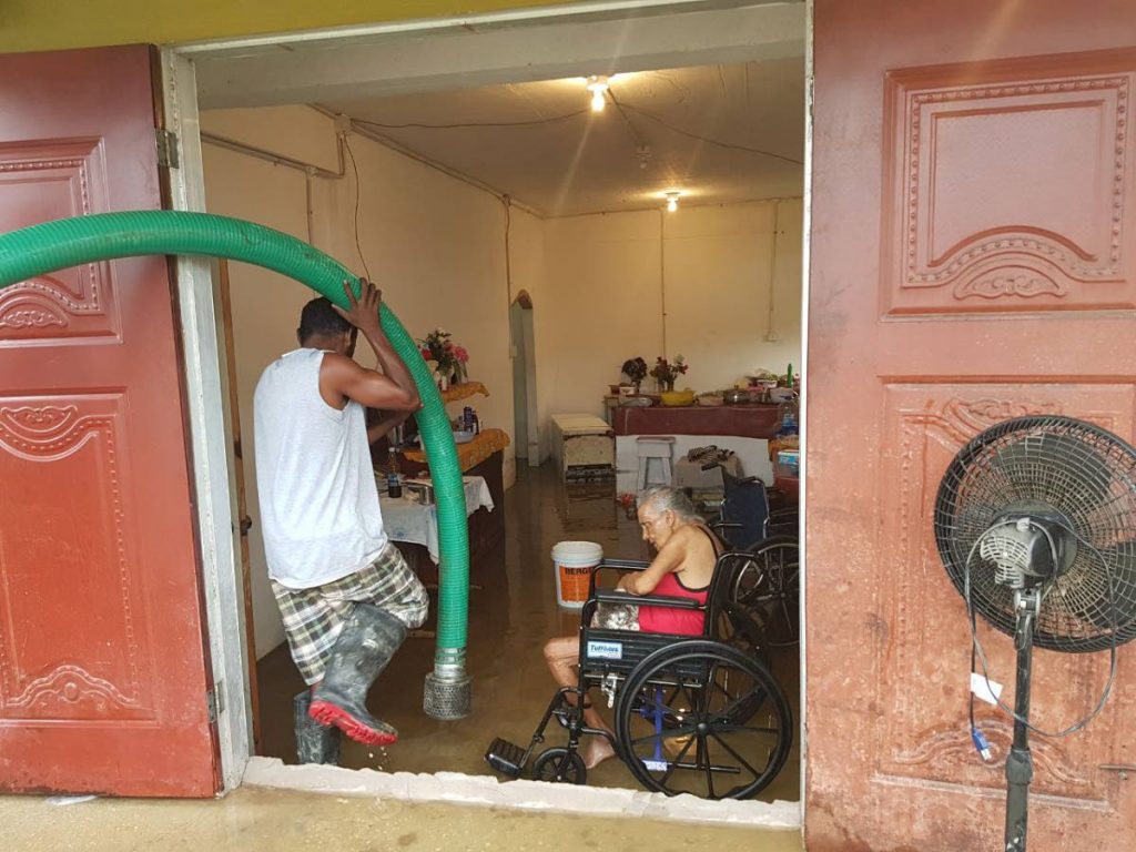 A nearby construction worker helps with the pumping out of water from the home of 82-year-old Jane Abraham in Bonasse, Cedros. 