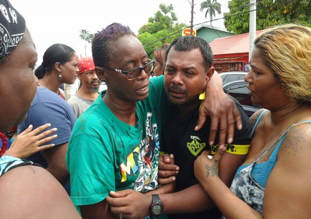 SORROW: Barbara Duncan Harris consoles Torrance Bedassie shortly after his mother Hannifa was found murdered in her shop in St Thomas Village, Chaguanas.