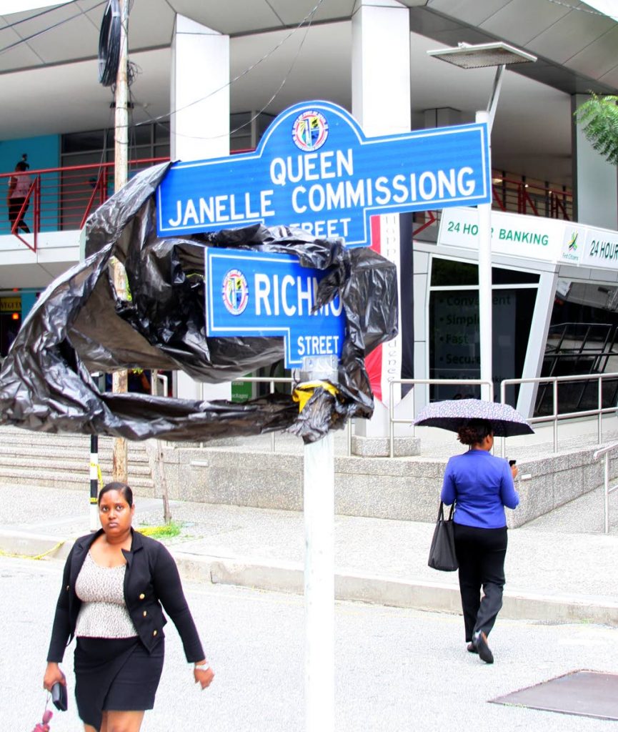ALL READY: Pedestrians walks past the new Queen Janella Commissiong street sign which from tomorrow replaces Queen Street in Port of Spain. 