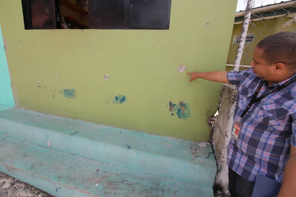 WILD WILD EAST POS: Newsday reporter Julien Neaves points to bullet holes on the front of a parlour at Plasiance Quarry Road, John John, Laventille. The bullets were from an exchange of gun fire between police and gunmen on Friday night.  