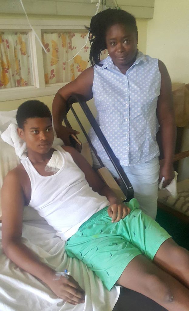 RECOVERING: Ophelia Faltine, mother of 15-year-old Joshua Faltine,left, stands at her son’s bed side yesterday at the Eric Williams Medical Sciences Complex, Mt Hope yesterday. Joshua was shot while in a maxi last Saturday along the PBR near to Beetham Gardens. PHOTO BY ROGER JACOB.