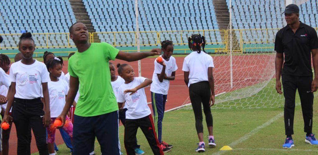 An aspiring athlete (centre) attempts a throw under the watchful eyes of 2012 Olympic javelin gold medallist Keshorn Walcott (right) at the Atlantic National Primary Schools Track and Field Development Camp, which was conducted at the Hasely Crawford Stadium, Mucurapo yesterday. 