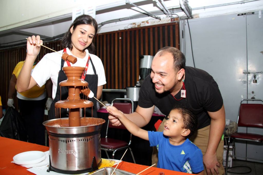 Hmm chocolate!: Rafael Escalante gets a little help from his father Matthew Escalante to cover a marshmallow with chocolate at the Cocoa Research Centre’s exhibition for World Cocoa and Chocolate Day at JFK auditorium, UWI, St Augustine yesterday. PHOTO by SUREASH CHOLAI