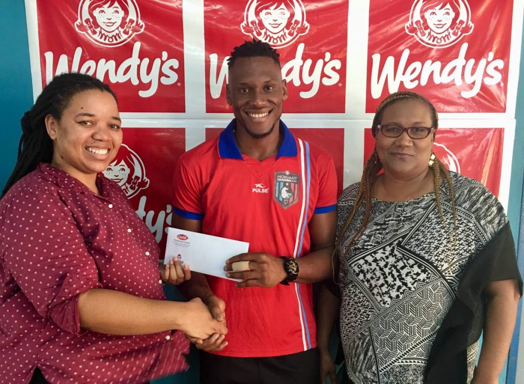 Sheyna Weston (left), marketing manager at Desk Restaurants – Wendy’s (Trinidad and Tobago) presents Morvant Caledonia United goalkeeper Glenroy Samuel with Wendy’s Pro League Player of the Month vouchers at the Ato Boldon Stadium in Couva on Wednesday. At right is TT Pro League general secretary Julia Baptiste. PHOTO COURTESY TT PROLEAGUE