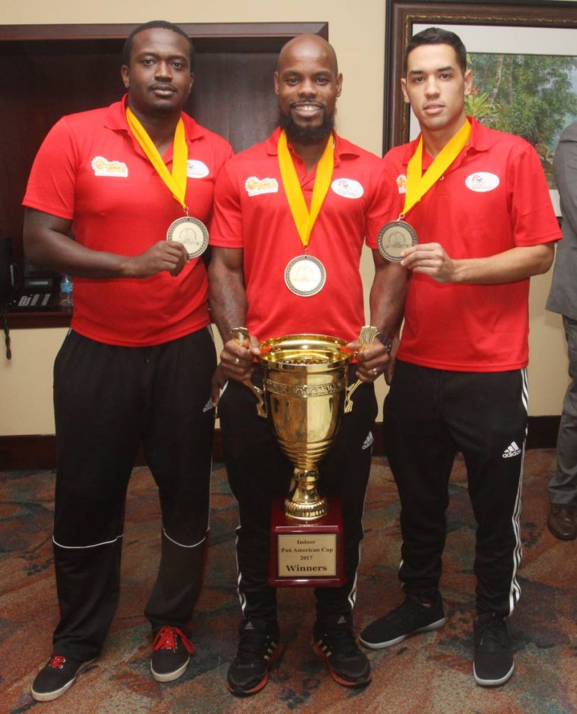 National hockey players Ron Alexander, left, captain Solomon Eccles, centre, and Jordan Vierra, show off the Pan Am Indoor trophy on their return home on Monday at the Piarco International Airport. 