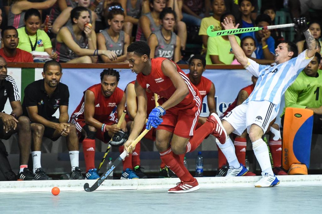 OUTTA MY WAY: Trinidad and Tobago’s Kristien Emmanuel, left, blows past his Argentine opponent in front the TT bench in the final of the Pan Am Indoor Hockey Cup in Guyana last week.