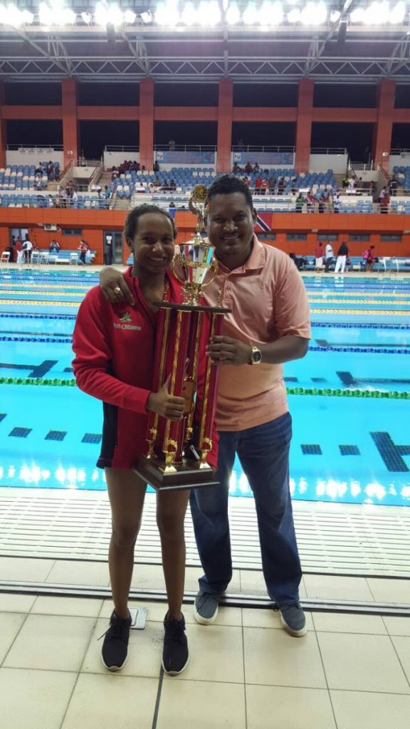 Sports Minister Darryl Smith, right, poses with TT swimmer Gabriella Donahue as she holds the 2017 CCCAN Overall Trophy which TT won at the National Aquatic Centre, Couva, in July.