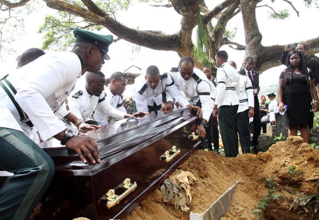 FAREWELL BATCH: Prison officers place the coffin of their murdered colleague Glenford Gardner at the graveside where he was buried at the Carenage Public Cemetery yesterday.  Looking on at far right is Gardner’s daughter Chelsea.
