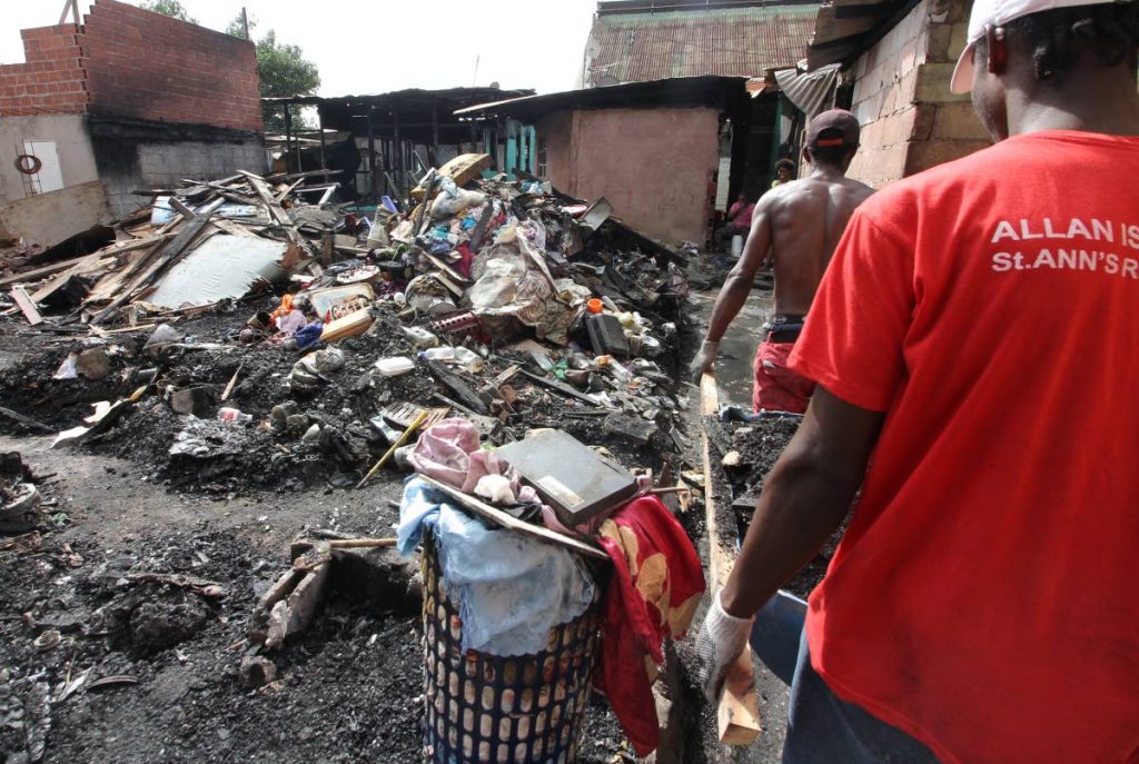 HELPING HANDS: Sea Lots residents assist their neighbours who lost their homes in a fire on Tuesday night.  Two men are seen removing rubble using a makeshift device made of wood and an old oil barrel cut in half.