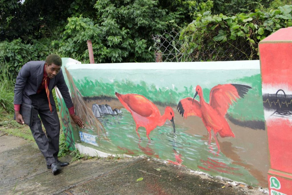 Artist Foster Isaac stands next to his mural of the Scarlet Ibis on a wall in Calder Hall.