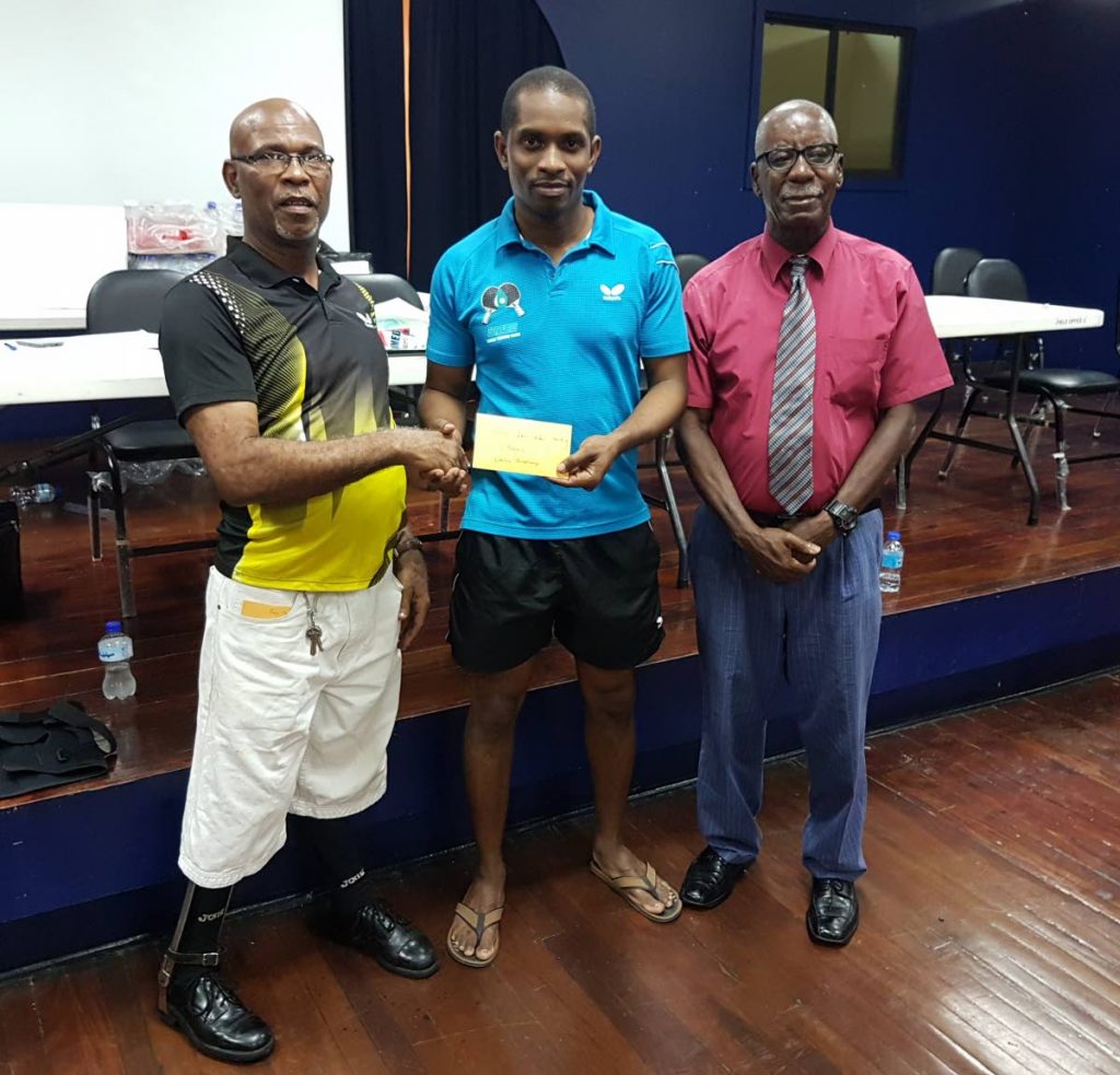 Curtis Humphreys, centre, receives a $1,000 prize from Dennis La Rose, left, after winning the Solo Crusaders“ Last Man Standing” table tennis tournament, at the PowerGen Sports Club in Port of Spain on Thursday night. At right is former Trinidad and Tobago and Crusaders coach Roland “Charlo” Charles.