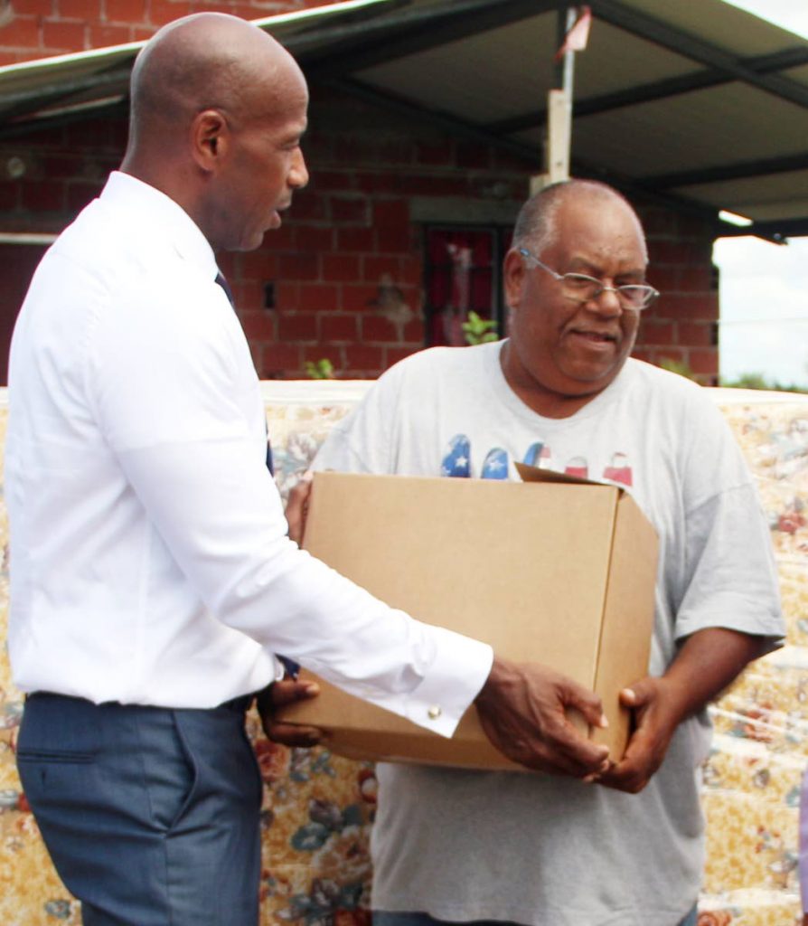 Darryl White of the Bankers 
Association presents a box of 
disaster relief supplies to Divali 
day flood victim Parasnath 
Raghubir on Wendesday in Avocat.