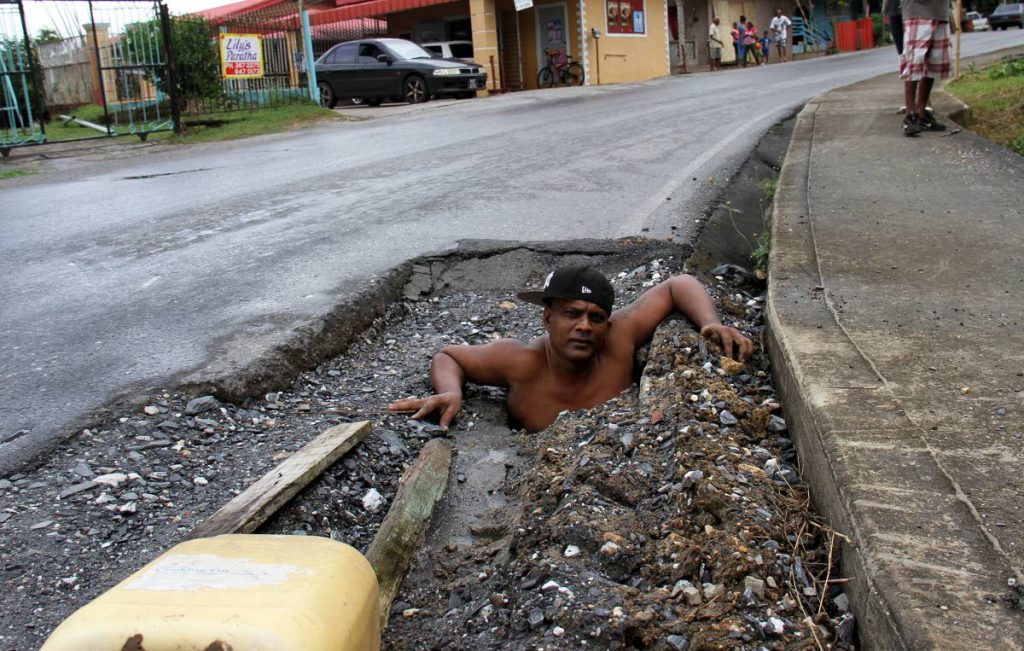 MAN IN HOLE: Sterling Chattergoon,  shows how large a hole is on Wellington Road, Debe. PHOTO BY ANIL RAMPERSAD.