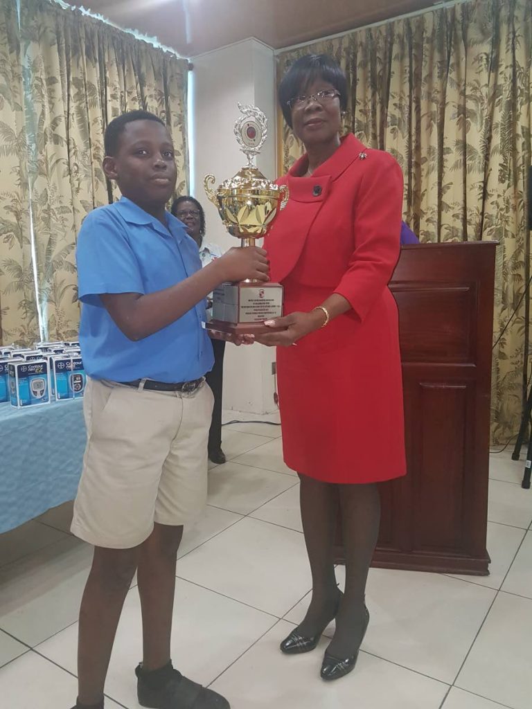  Rondell Daniel of Delaford Anglican Primary School collects his prize from Dr Agatha Carrington, Secretary for Health, as a participant in the 6-9 age group in the drawing category of the World Diabetes Day poster competition hosted by the Bovell Cancer Diabetes Foundation.