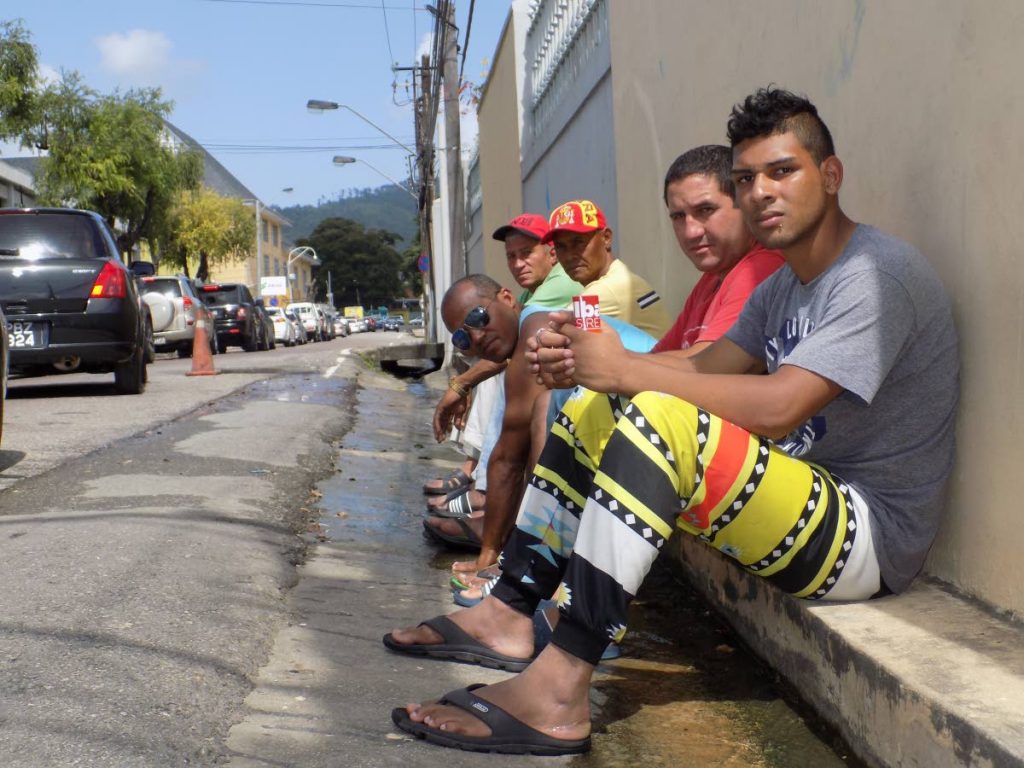 File Photo: Yusnell Perez, first from right and four other Cuban nationals sit over a drain just outside the United Nations Regional Office at Chancery Lane, Port of Spain.  PHOTO BY SHANE SUPERVILLE