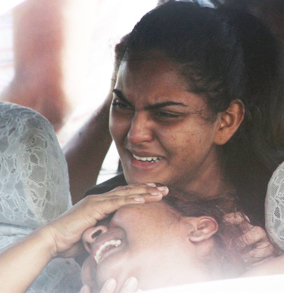 SUNDAY SORROW:Shivana Roodal, top, consoles her weeping mother Maltie yesterday after the body of Shivana's father and Maltie's husband Pooran Roodal was found in his car with a stab wound to his neck in Kelly Village, Caroni.