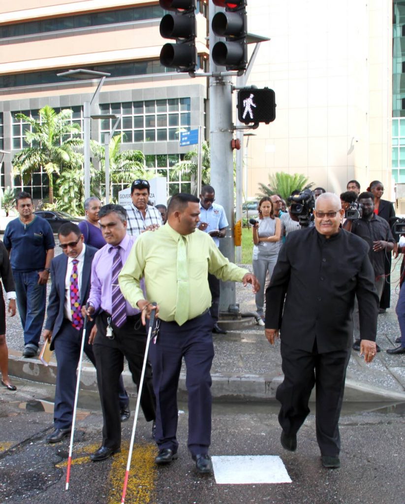 File photo: Works and Transport Minister Rohan Sinanan (left) escorts Blind Welfare Association members Lakhan Seepersad, Kenneth Surrat and Patrick Romano (president) across Wrightson Road after the commissioning of upgraded traffic lights to assist the hearing and visually impaired.   PHOTO BY SUREASH CHOLAI