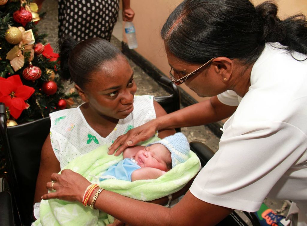 Midwife Rookmin Pirmal assists Nikibah Myler who cradles her newborn son yesterday at the San Fernando General Hospital.