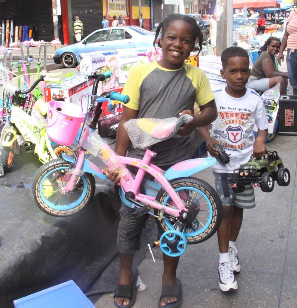 More gifts?: Two boys carry a bike and toy car perhaps hoping to get more Christmas gifts as shoppers came out for Boxing Day bargains in Port of Spain yesterday. Photo by Angelo Marcelle