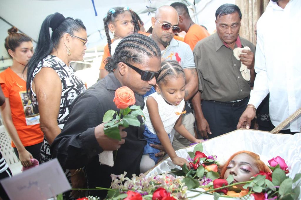 SHE’S GONE: Brian David holds his niece Irisa as she places a flower next to her mother Arisa David at the funeral held at Limehead Road, Chase Village yesterday.