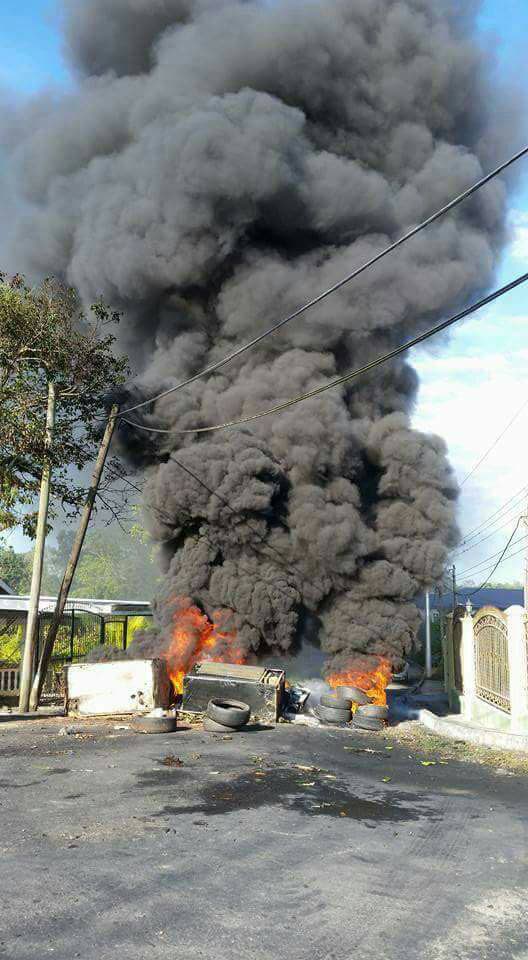 Smoke from burning debris fills the air as residents of Sixth Company Village in New Grant protested over the poor condition of the road.