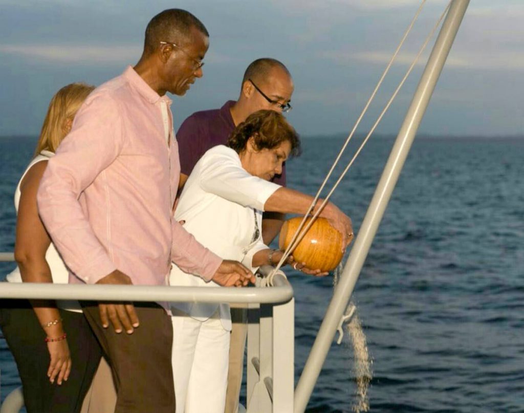 Dr Jean Ramjohn Richards pours the ashes of her husband, the late president George Maxwell-Richards, into the sea as CEO of Belgroves Funeral Home Keith Belgroves, right, her son Mark, and daughter Maxine (at back) support her aboard the TTS Moruga, on the Gulf of Paria, off San Fernando at sunset on Friday. Photo courtesy Curtis Khan
