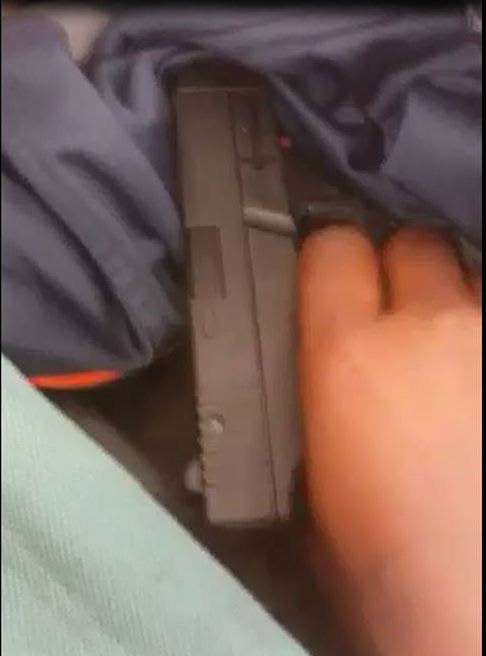 A screenshot of a video in which secondary school students show what appears to be a .9mm pistol.