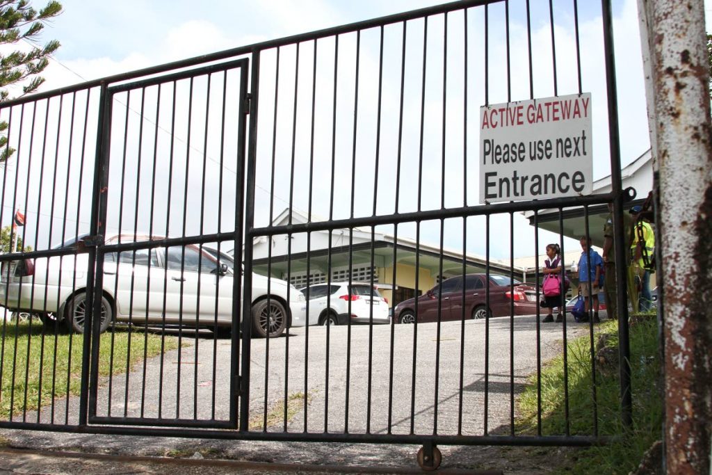 Child protection: Students wait behind a locked gate at Jordan Hill Presbyterian Primary School, Princes Town under the watch of a security guard last week. Only one entry and exit is in use after a gunman robbed a teacher on the compound on February 21. PHOTO BY JEFF MAYERS