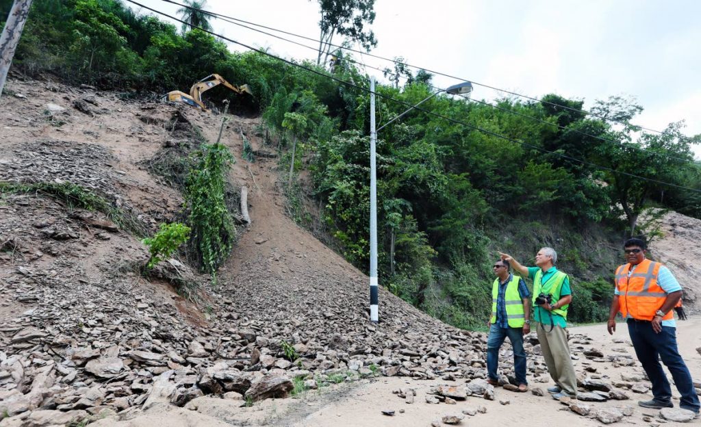 Major works: Minister of Works and Transport Rohan Sinanan, left to right, engineer Dr Derek Gay and acting Director of Highways Navin Ramsingh, look on as an escavator works on a ridge along Lady Young Road yesterday. The road is due to reopen on Monday after a landslip this week. PHOTO BY AZLAN MOHAMMED