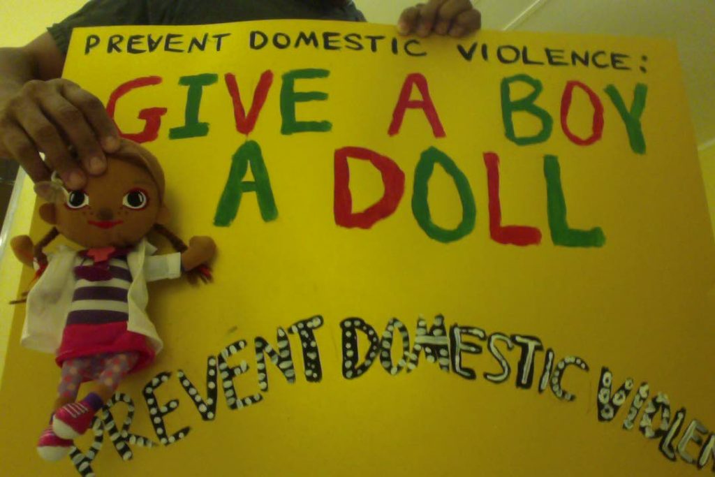 A poster reads Give a boy a doll--in an anti-domestic violence message.