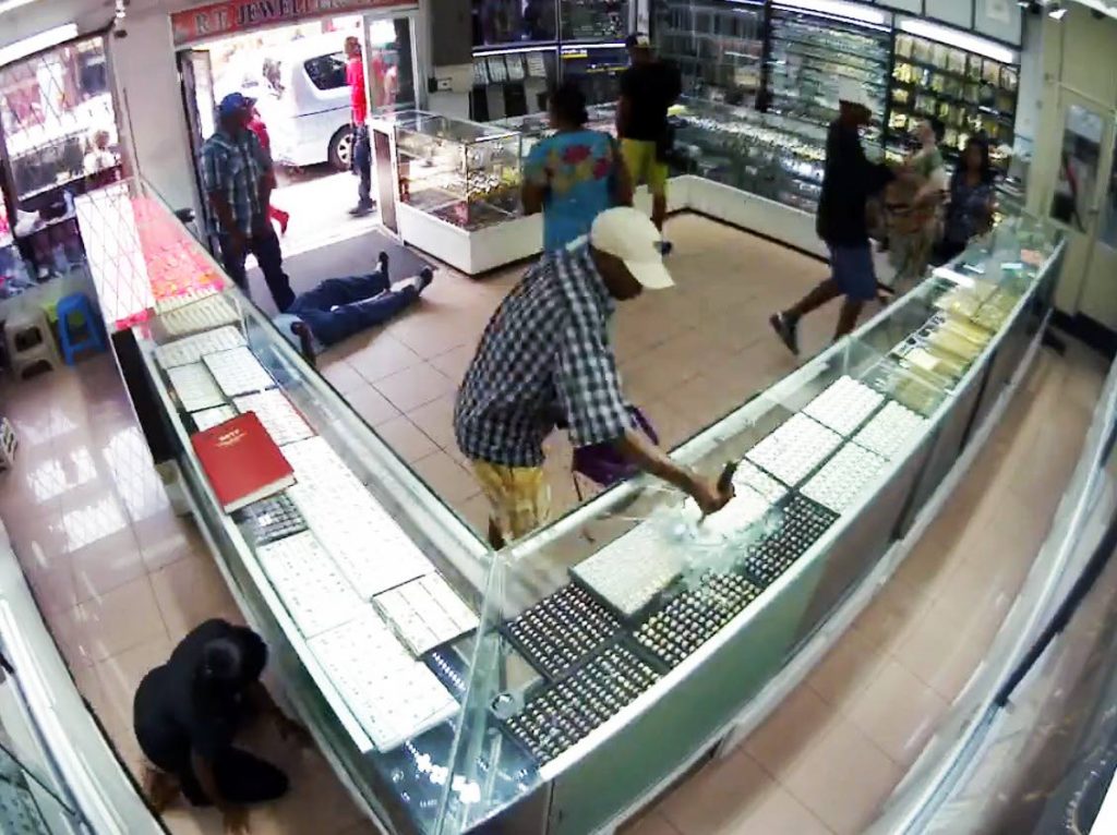 Hammer time: This freeze frame,
taken from CCTV
images posted to social media, shows a clerk cowering in fear as three bandits held-up a jewelry store during broad daylight on High Street in San Fernando yesterday. One of the men is seen using a hammer to smash
the showcase to get to the jewelry.