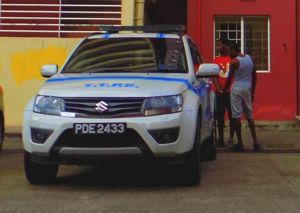 Two men stand near a police vehicle after they were arrested by officers of the PoS CID during an eviction exercise at Clifton Towers in East PoS, yesterday.