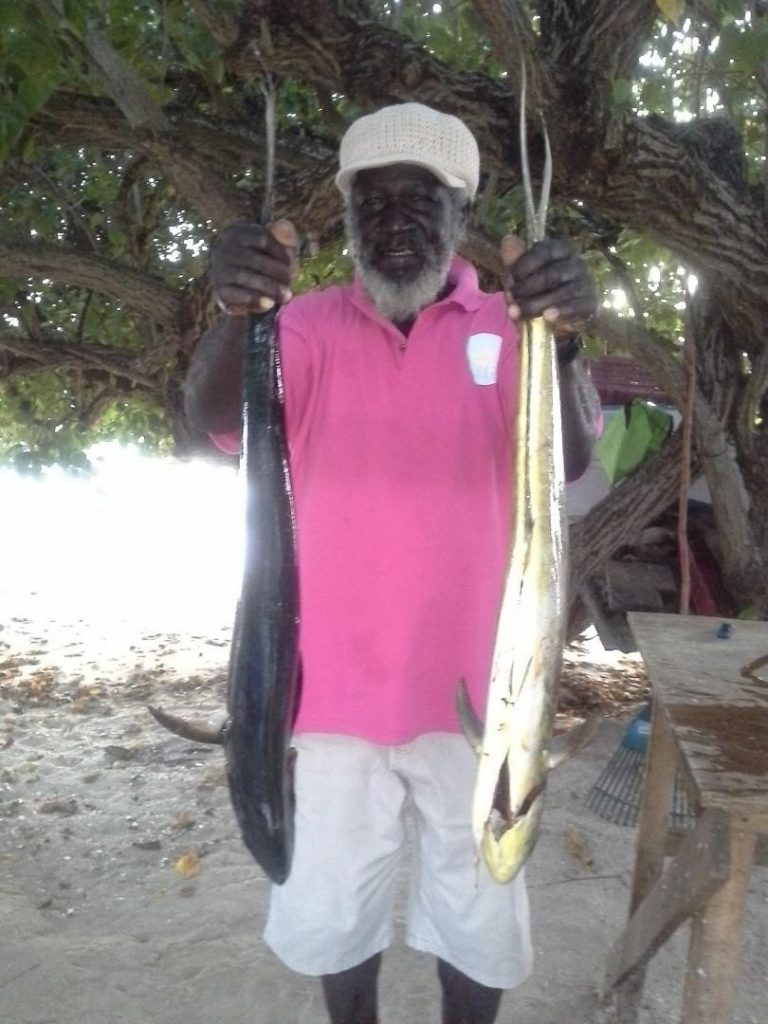 Fisherman Fitzroy Burnette of Canaan, poses with two dolphins from his catch of the day, next to his fish stall at the Swallows beach on the Pigeon Point Road in Crown Point.

