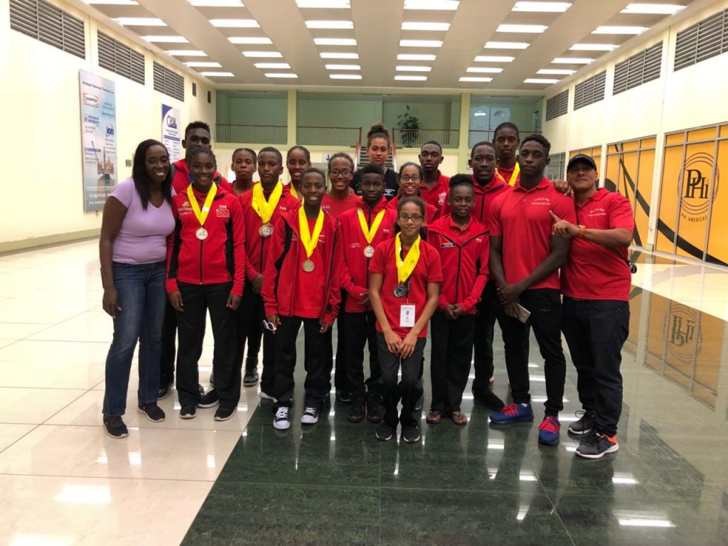 National swimmers pose with chaperone Ann Thompson, left, and assistant coach Dexter Browne, right, on their return to Trinidad on Wednesday evening at the Piarco International Airport.

