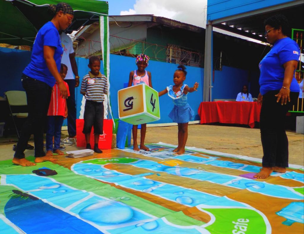 Zap that Mosquito: A girl throws the dice during a life-sized game of Zap that Mosquito, a variation of Snake and Ladders designed by the TT Red Cross to raise awareness about the Zika virus, during the children's health fair at the Kind compound in Laventille last Thursday. PHOTOS BY SHANE SUPERVILLE 