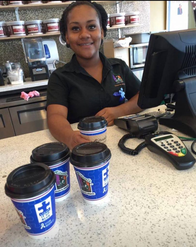 An employee at Rituals in Maraval distributes Light It Up Blue coffee cups to raise awarenes for autism. 