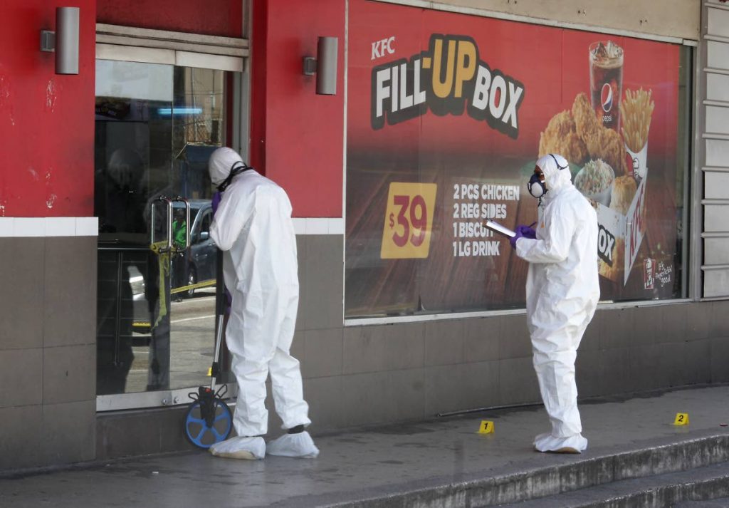 DEATH SCENE: Investigators process the area where a man was stabbed to death during a scuffle with a security guard at the Independence Square, Port of Spain branch of KFC yesterday.