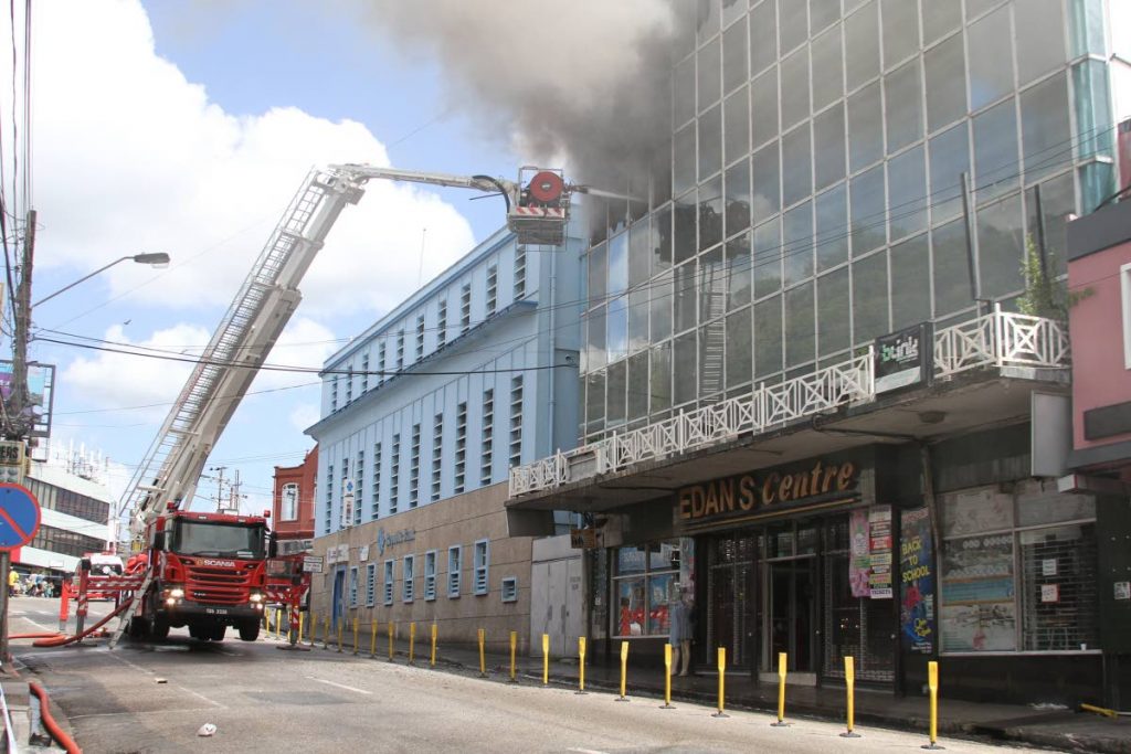 ON FIRE: Firemen use a hydraulic ladder to reach the top floor of the Edan’s Centre to fight a fire in the Edan’s Centre in San Fernando.