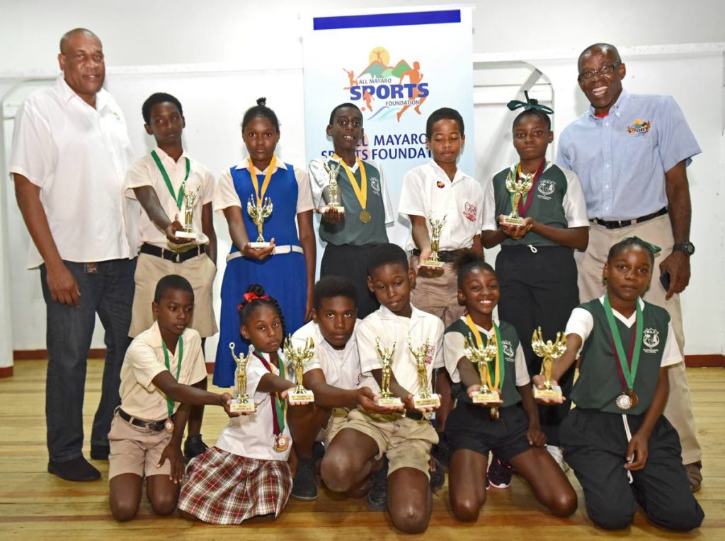 Winners of the Victor and Victrix Ludorum titles in various age categories of the Mayaro Primary School Zonal Athletic Games proudly show off their medals as Bartholomew Lynch (left), Chairman, AMSF, and Matthew Pierre (right), Community Liaison Officer, BPTT, celebrate with them.