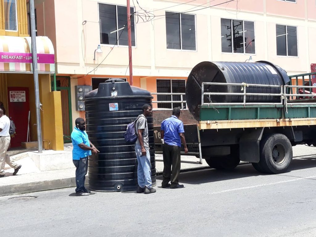Workmen load water tanks onto a truck on Wilson Road, taken from the Scarborough market opposite, on Tuesday morning.  The tanks were removed, cutting off the water supply to the market,  while vendors were inside the facility engaged in protesting a sudden Saturday deadline to relocate to the temporary market facility at Shaw Park .The water tanks were taken for installation at the Shaw Park facility.