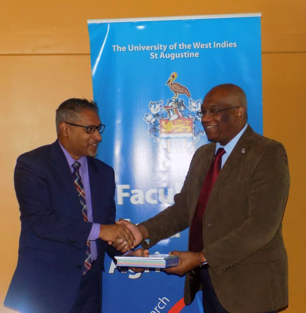 Minister of Agriculture, Land and Fisheries Clarence Rambharat, left, receives a book from UWI Campus Principal Professor Brian Copeland during a Food and Nutrition Security Symposium at the UWI Inn and Conference Centre this morning. 