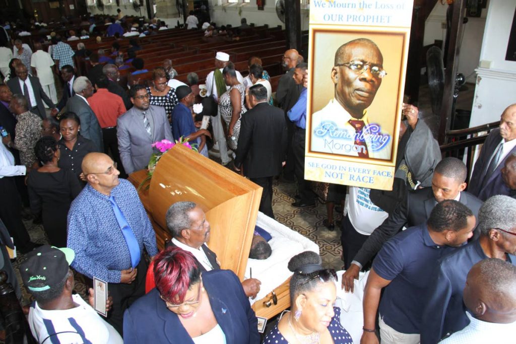RIP: A large portrait of Dr Morgan Job is held high by a man at his funeral held at the Holy Trinity Cathedral in Port of Spain yesterday as hundreds file pass his casket.