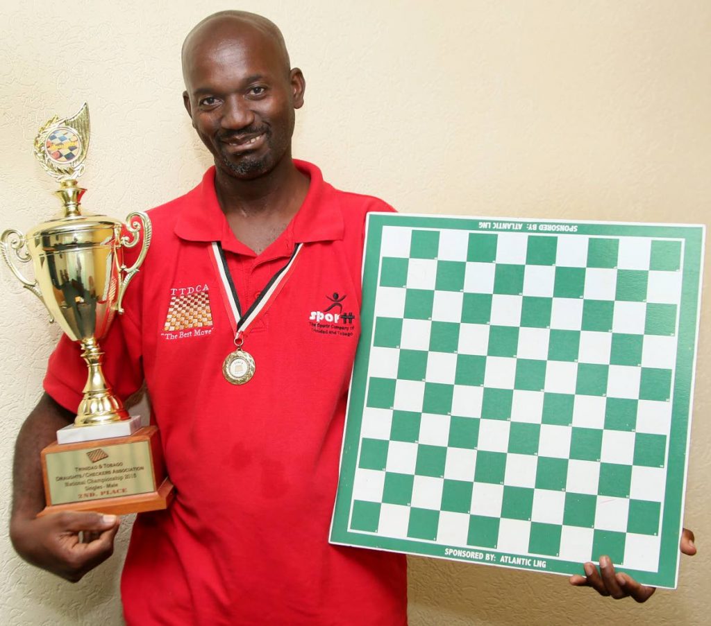 Anderson Charles, with his trophy and a draughts board, during a visit to Newsday’s Port of Spain office on Wednesday.