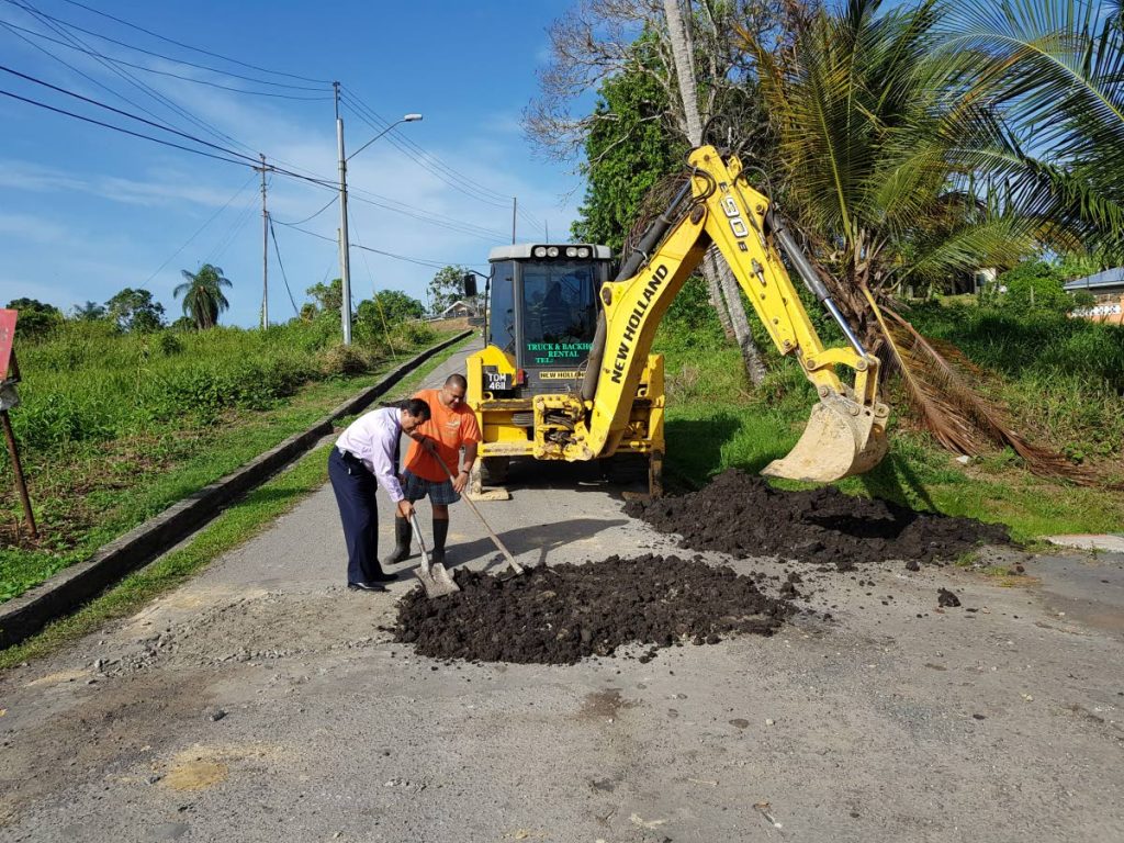 SELF HELP: Fyzabad MP Dr Lackram Bodoe assists Sewlal Trace, Fyzabad resident and coordinator Kierron Yip Ngow in spreading some material to fix the road which has been in a deplorable condition for sometime.