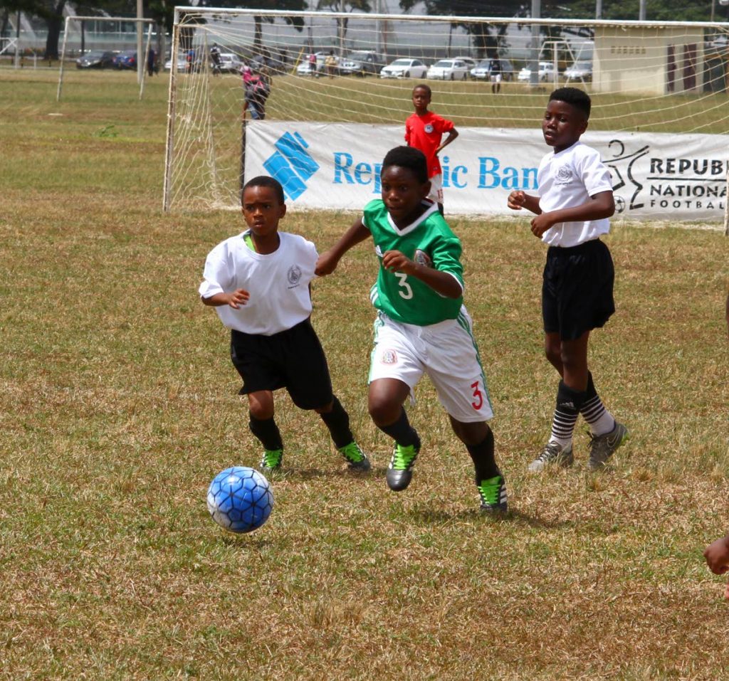 Jerrel Joefield, centre, of Elite 123 Goodness FC on the attack against Rosary Boys RC yesterday at the Queen’s Park Savannah, Port of Spain.