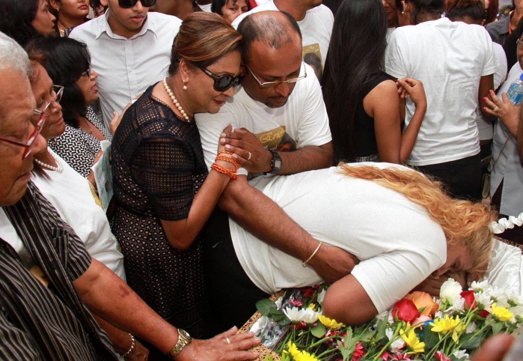 Opposition Leader Kamla Persad Bissessar hugs Vishnu Ganesh while his wife Waheeda leans over the coffin with their son Eric Ganesh during his funeral service, which took place at St. Charles Village, Princes Town. 
PHOTO BY ANIL RAMPERSAD.