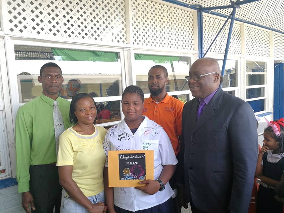 Carissa McPherson, centre, of the Black Rock Government Primary school, who seventh in the Secondary Entrance Assessment (SEA) exam, stand with Chief Secretary Kelvin Charles, right, and others at the school on Wednesday.