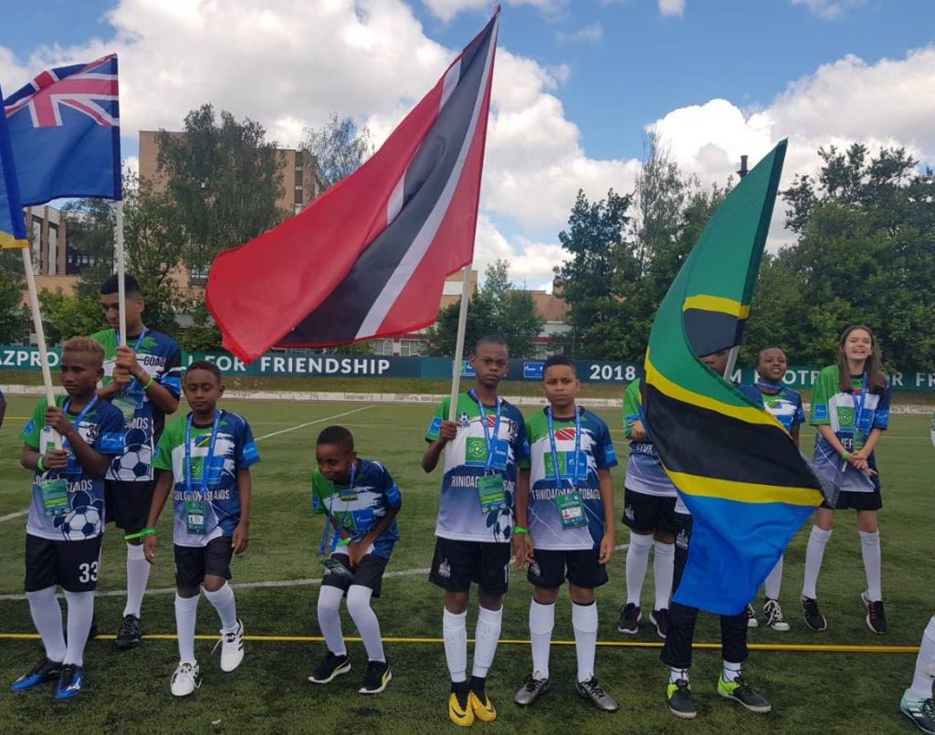 TT reps: Khileal Remy-Gould stands alongside Kyle Phillip, who holds the national flag, as they represented TT at the Football For Friendship International Youth Forum, Russia, where they also saw the opening 2018 World Cup match between Russia and Saudia Arabia on June 14. 