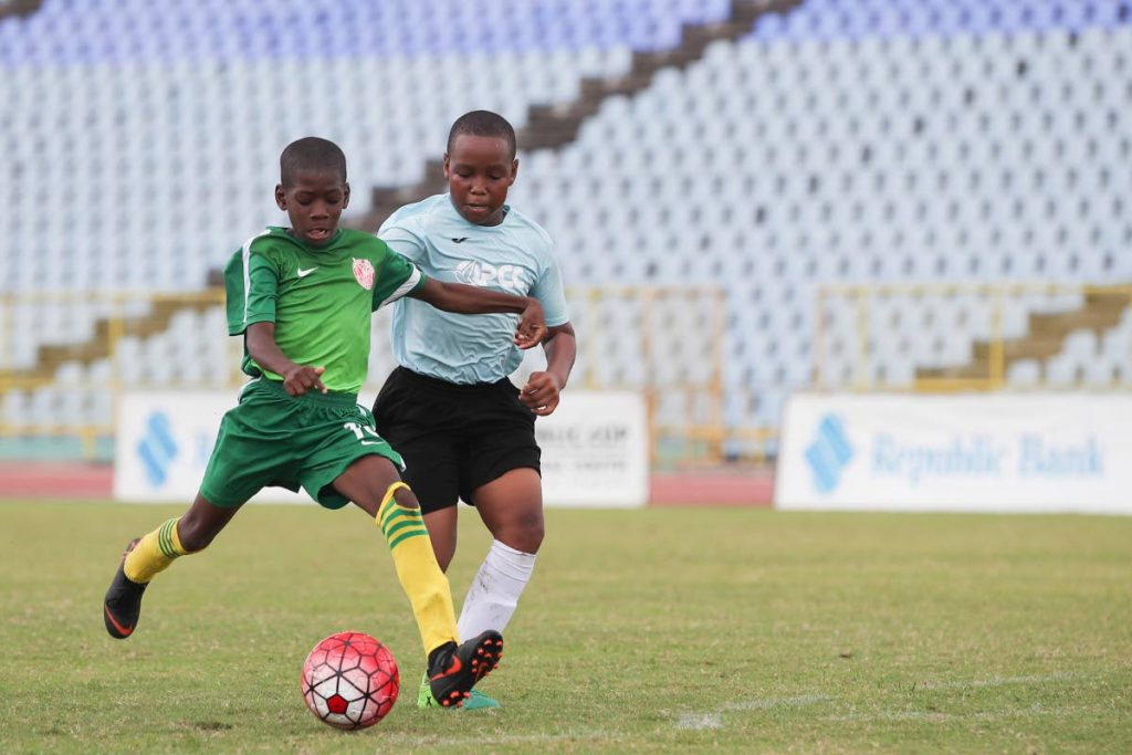 In the U12 division, Trendsetter Hawks goal scorer Antonio Sealey (green) has a shot on goal with QPCC defender Matthew Barrington on his trail, during the finals of the Republic Bank Youth Cup at the Hasely Crawford Stadium, Mucurapo.  Trend Setters won 2-1.
